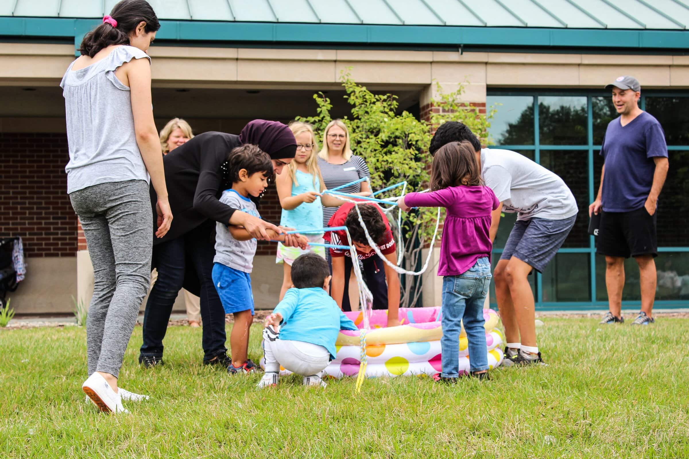 Several children with their parents playing in a kiddie pool outside the library.